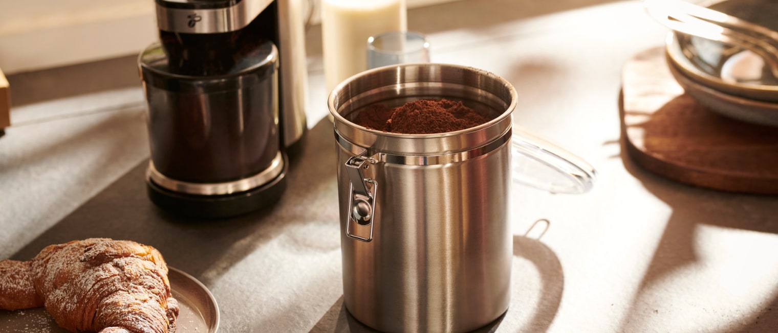 Eine Kaffeedose steht neben einer Kaffeemühle auf einem Tisch','Enter picture alt'}