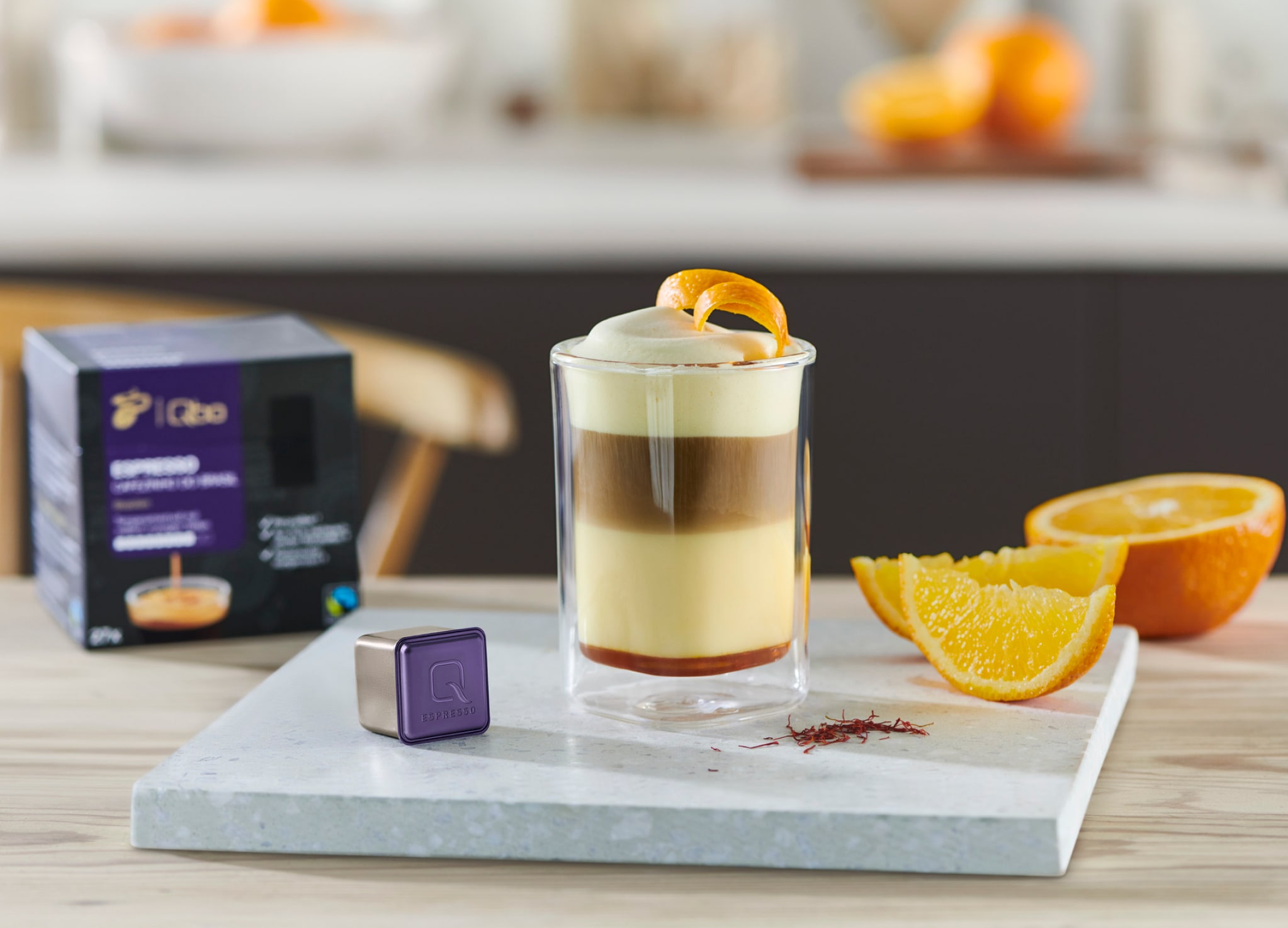 Glas Kaffee steht mit Qbo Kapseln und einer geschnittenen Orange auf dem Tresen
