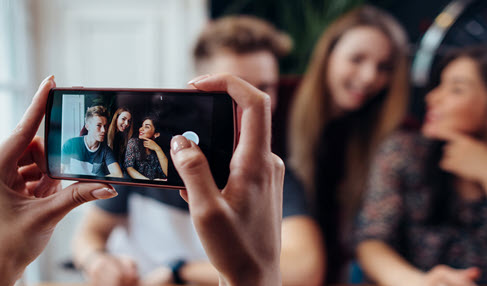 Frau, die mit dem Smartphone ein Foto von ihren lachenden Freunden macht.
