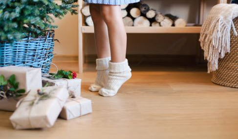 Ein Mädchen stellt sich in ihren weißen Kuschelsocken auf die Zehenspitzen vor einen Weihnachtsbaum.