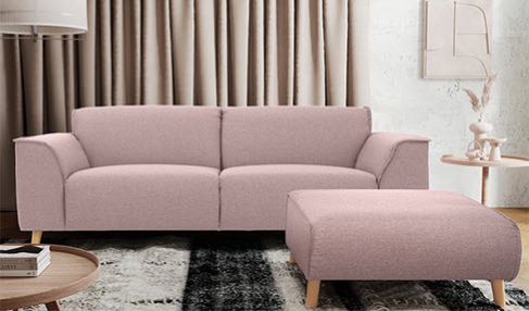 Ein hellrosa 2-Sitzer aus Wildleder steht in einem Wohnzimmer vor einer beigen Gardine.