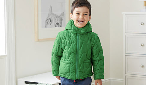 Ein kleiner junge in einer grünen Daunenjacke strahlt in die Kamera.
