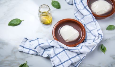 Qualitätssiegel sorgt für Wohlbefinden: Um eine Schüssel mit Burrata liegt ein weiß-kariertes Küchenhandtuch.
