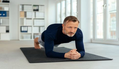 Ein Mann macht zu Hause auf einer Matte Fitnessübungen und trägt dabei ein dunkelblaues Sportshirt mit langen Ärmeln.