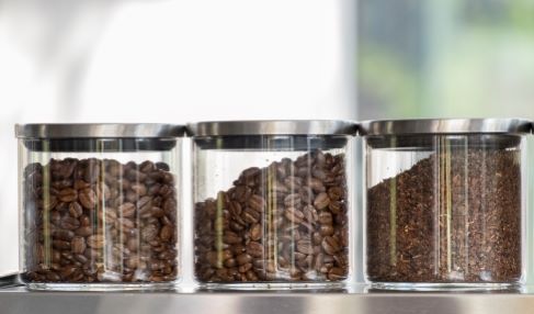 Gut gelagert: Auf einem Regal stehen drei Glaskontainer gefüllt mit Kaffeebohnen und Kaffeepulver.