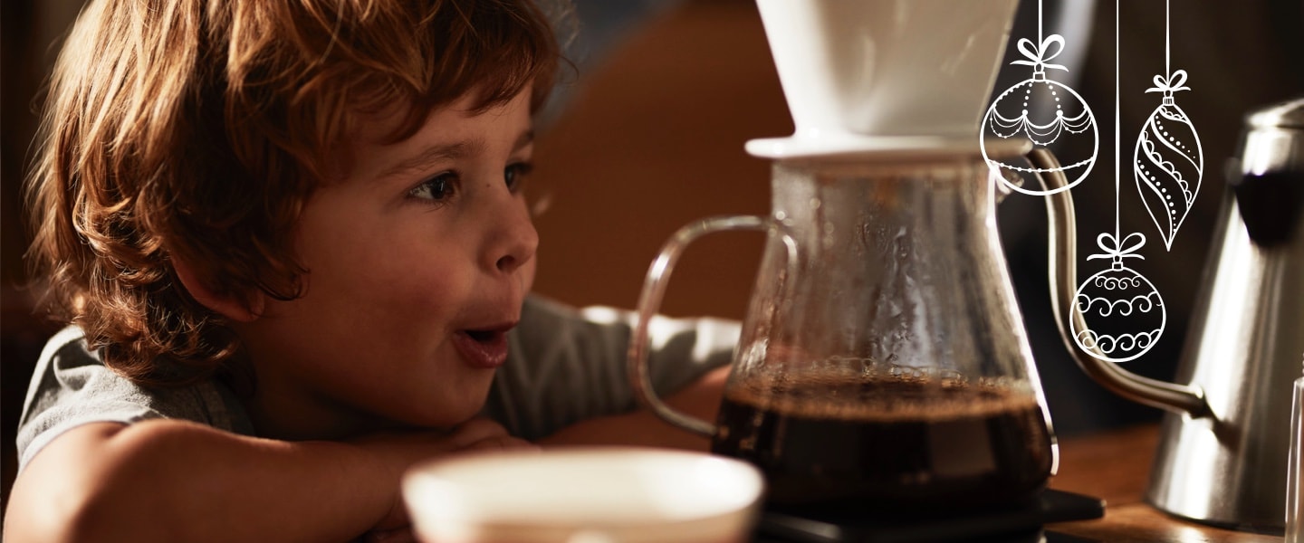Ein kleiner Junge schaut zu, wie ein Kaffee mit einem Keramikfilter in eine Glaskanne aufgebrüht wird. Das ist die Schwerpunkt Seite der Manuellen Zubereitung.