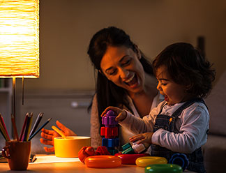 Warmes Licht im Kinderzimmer: Eine Mutter spielt mit ihrem Kleinkind im Schein einer Tischlampe, die warmes schummriges Licht ausstrahlt.