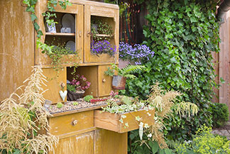 Ein Gartenschrank schafft Ordnung: Holzschrank in Vintage-Optik dient als Ordnungs- und Deko-Element im Garten.