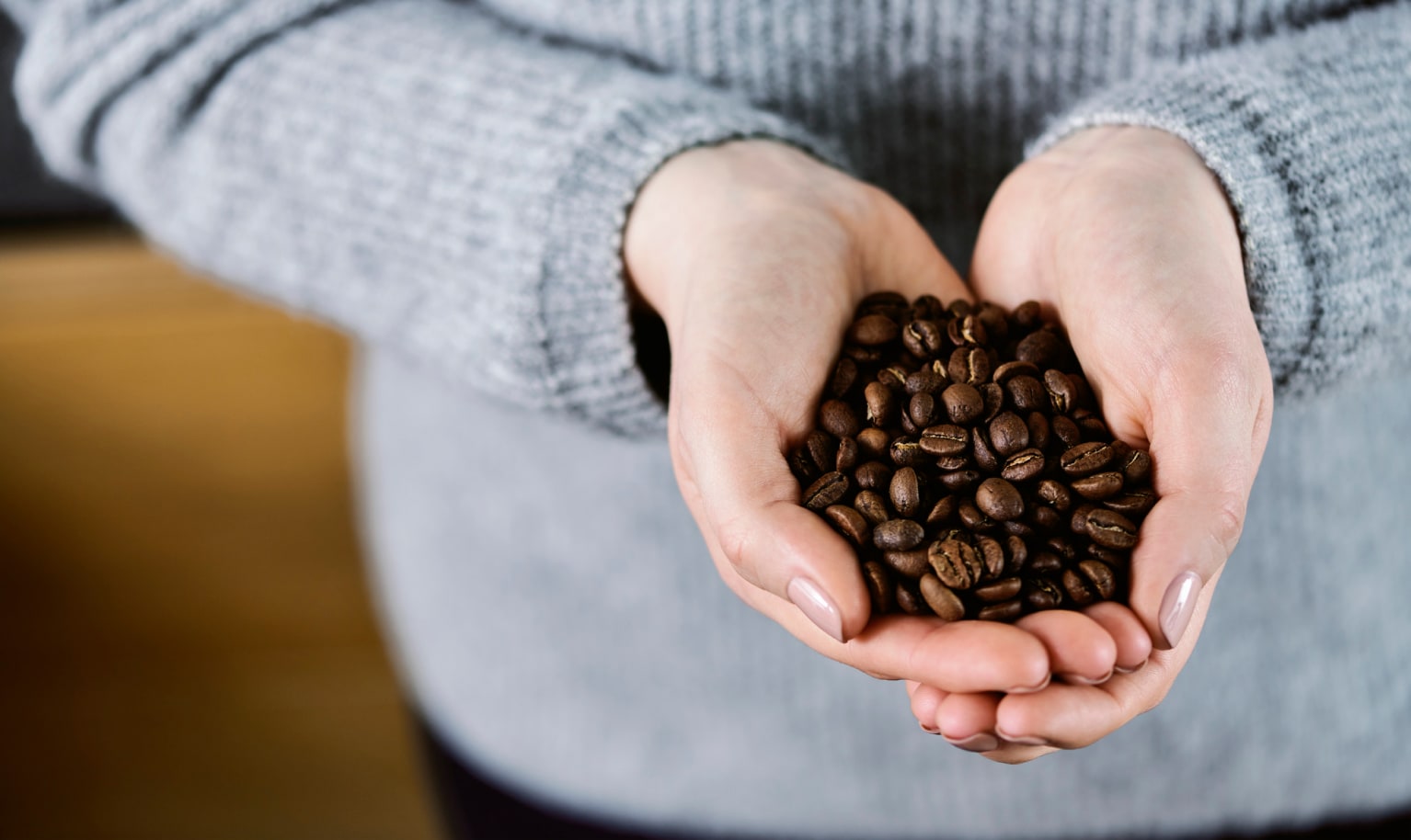 Jemand hält beide Hände voller Kaffeebohnen in die Kamera