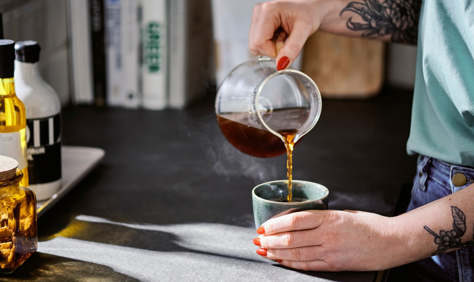 Jemand schenkt sich Filterkaffee aus einer Glaskanne in einen Becher ein.