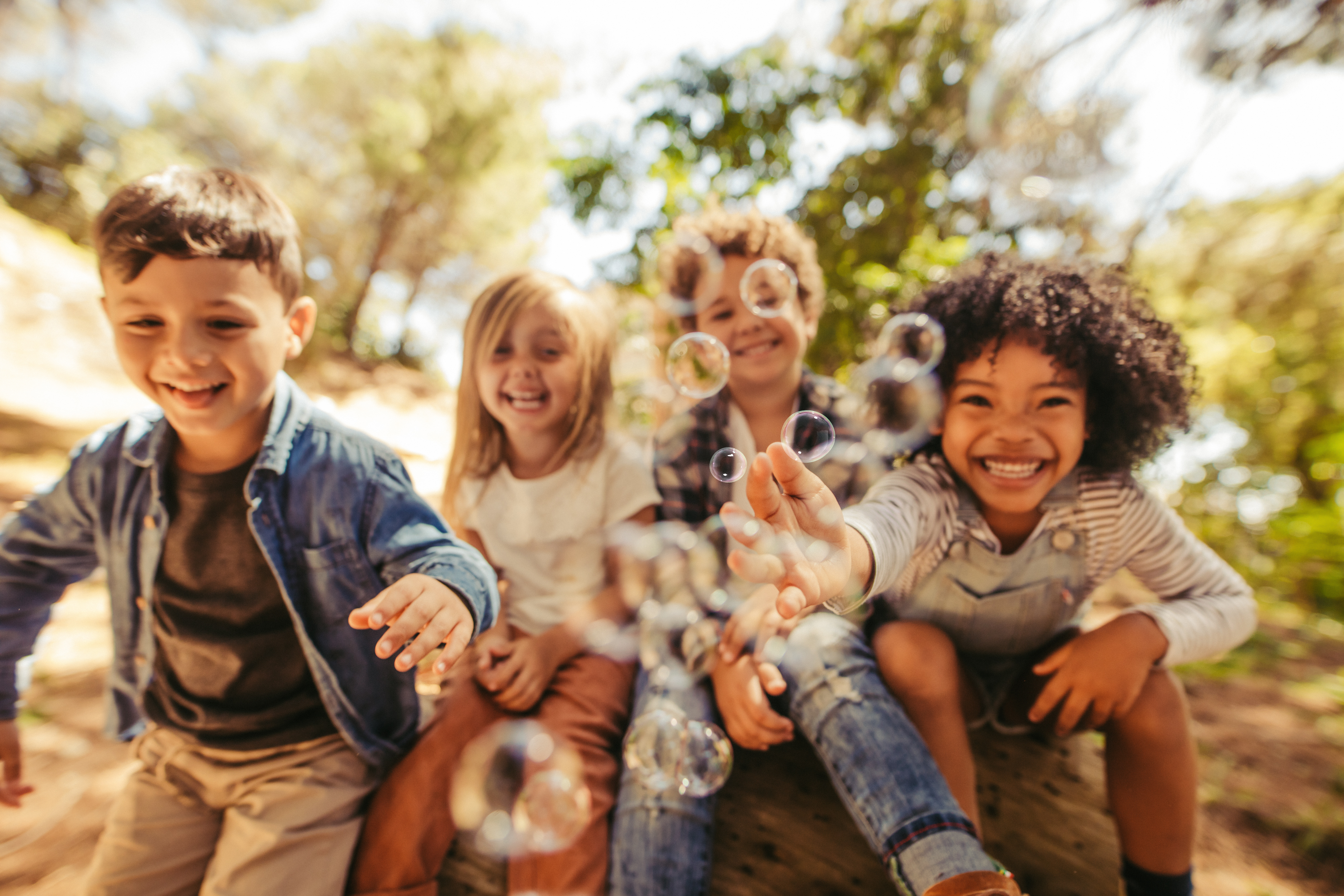 Vier Kinder schauen lachend in die Kamera und spielen mit Seifenblasen.