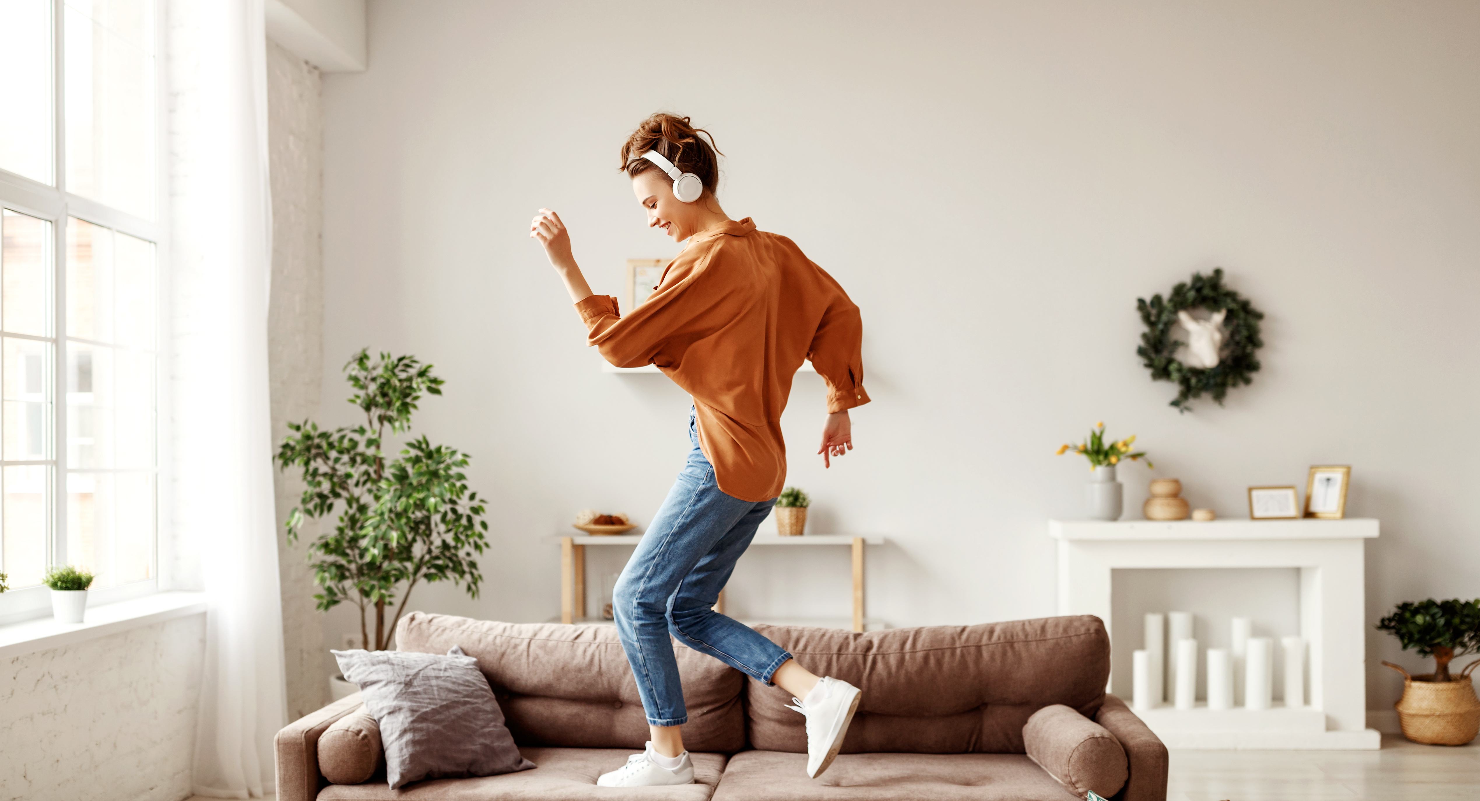Frau tanzt zu Hause auf ihrem Sofa mit On-Ear-Kopfhörern.