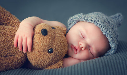 Ein Baby schläft gemütlich mit einem Teddybär im Arm.