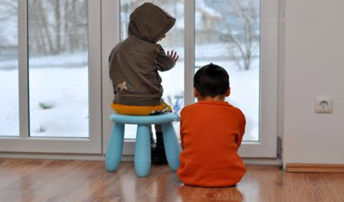 Vor einem Fenster sitzen zwei kleine Jungen auf einem Kinderhocker.