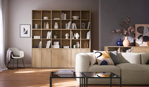 Ein helles Sofa steht in einem modernen Wohnzimmer. Dahinter steht ein großes offenes Regal aus Holz.