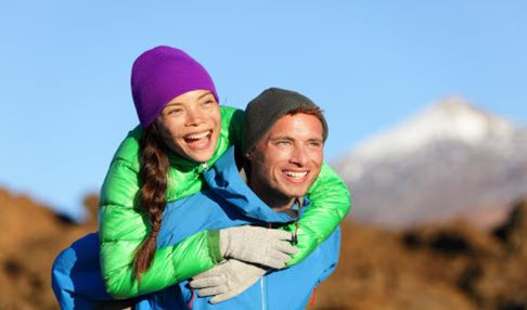 Gut ausgestattet: Eine Frau in grüner Daunenjcke und ein Mann in blauer Outdoorjacke gehen wandern und sind dafür mit guter Funktionswäsche ausgestattet um warm zu bleiben.