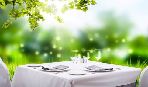 Im Garten steht ein gedeckter Tisch mit einer weißen Tischdecke. Der Tisch ist gedeckt.