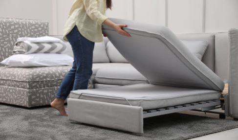 Eine Frau baut ein graues Schlafsofa auf.