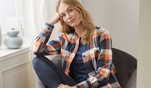 Eine Frau trägt eine orange blau karierte Hemdbluse und sitzt auf einem dunkelblauen Sessel