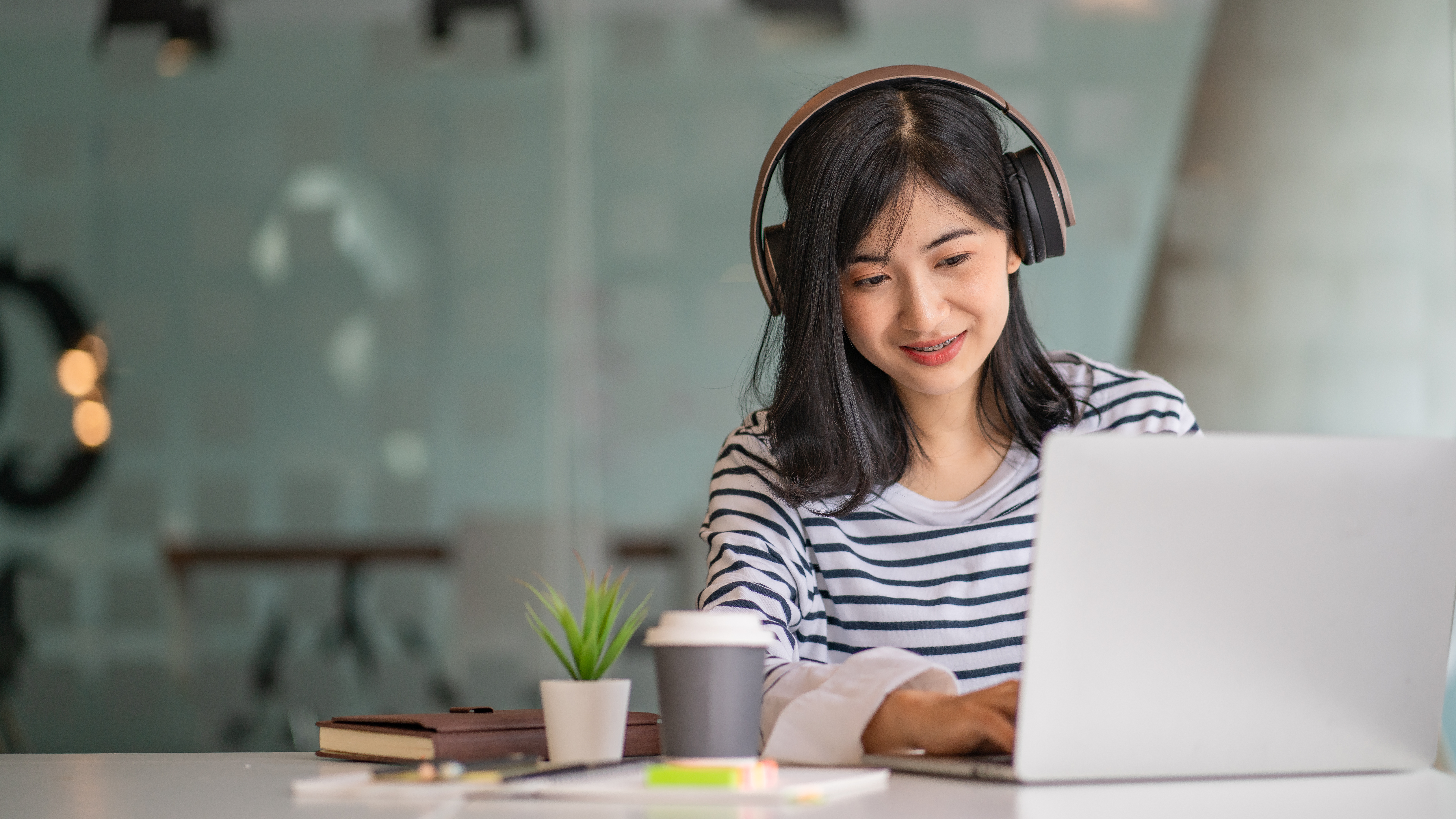 Frau, die an einem Laptop sitzt und Musik über On-Ear-Kopfhörer hört.