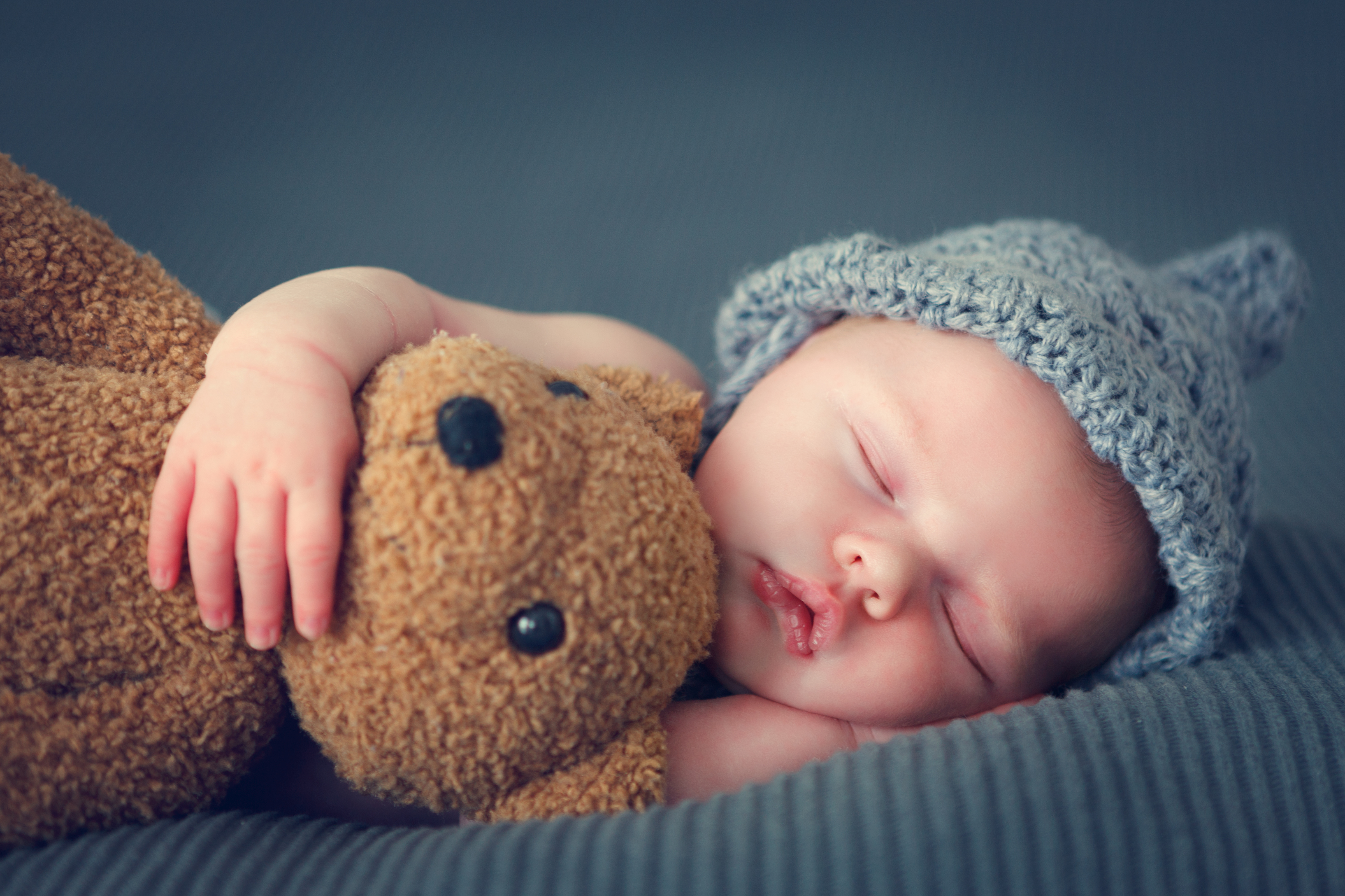 Ein Baby schläft gemütlich mit einem Teddybär im Arm.
