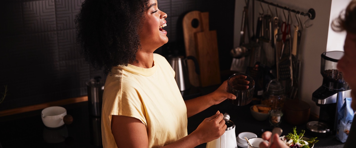 Ein stimmungsvolles Bild einer lachenden Frau, die ihren Kaffee zubereitet leitet den Einstieg auf die Kaffeemaschinen und -bereiter Seite ein. Entdecken Sie hier für jede Zubereitungsart die passende Maschine.