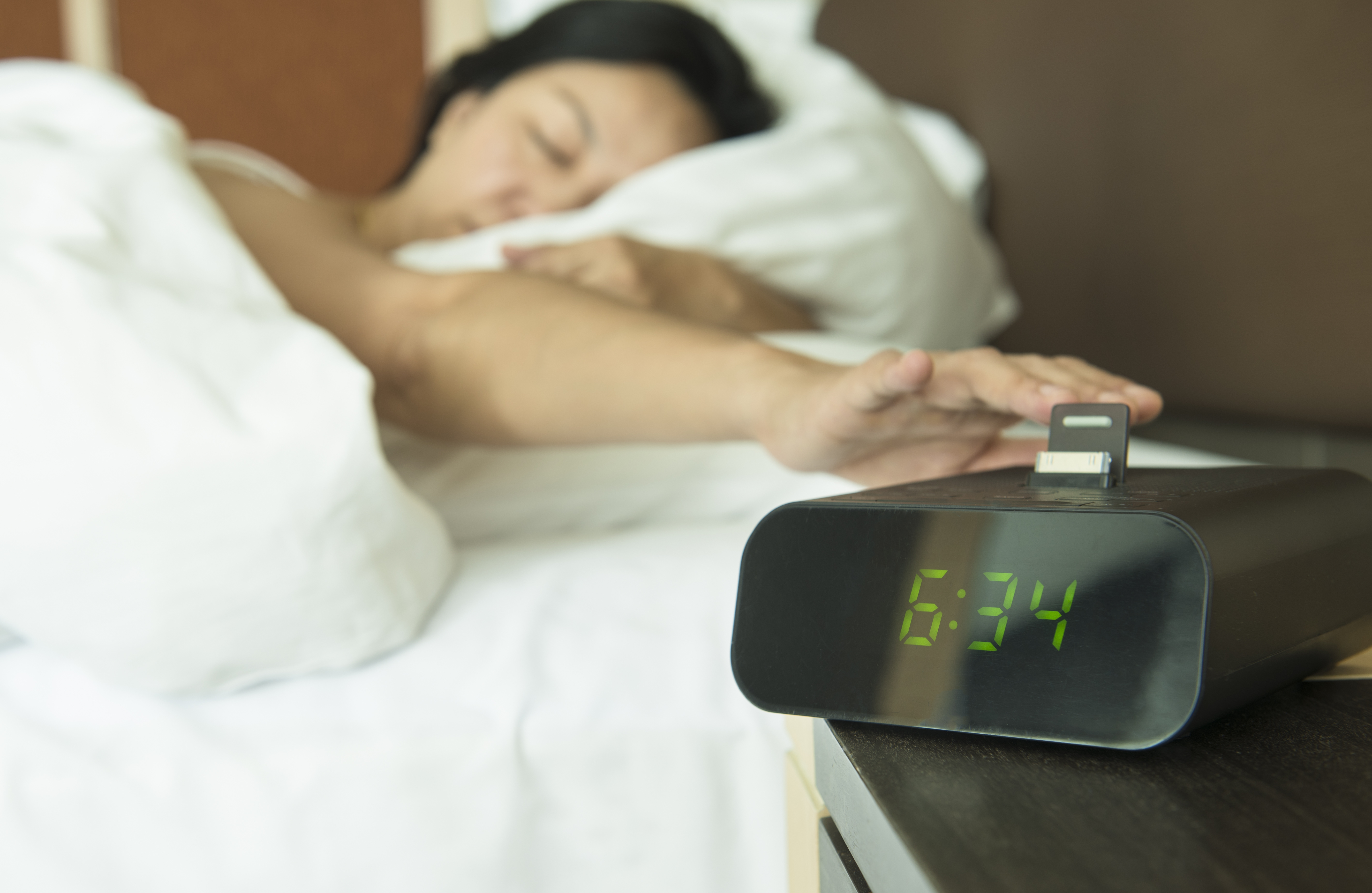 Frau drückt im Halbschlaf auf ihren Wecker, der neben dem Bett steht.