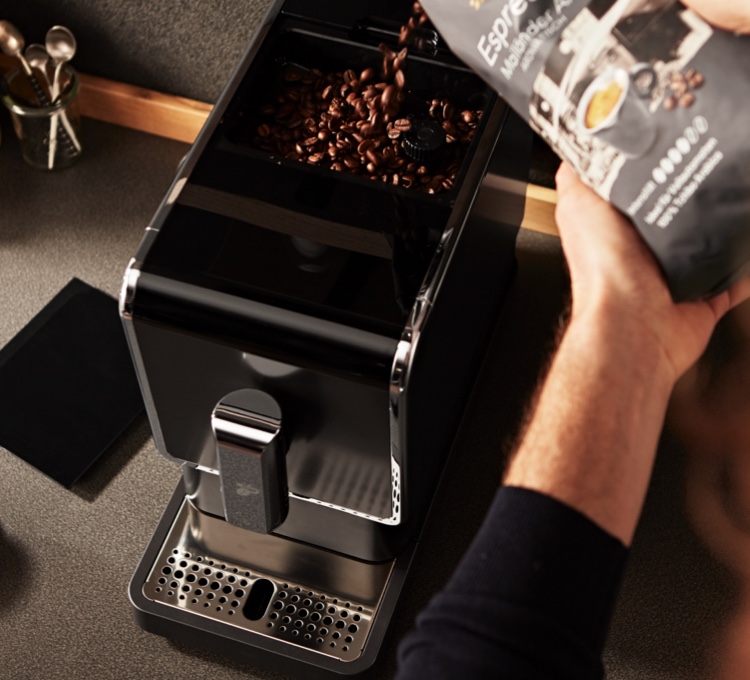 Stimmungsvolles Bild, wie Ganze Bohne Kaffee in einen Vollautomaten gefüllt wird. Kaufen Sie den passenden Kaffee für Ihren Vollautomaten.