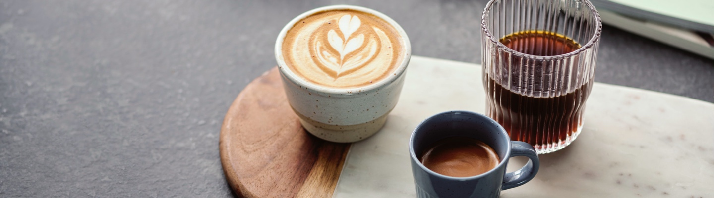Specialty Coffee von lokalen Röstereien stehen zubereitet als Cappuccino. Espresso und Filterkaffee auf einem Holztablett auf der Küchentheke.