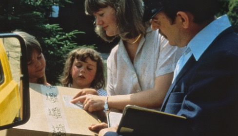 Postbote der 50er Jahre übergibt Familienmutter ein Tchibo Paket
