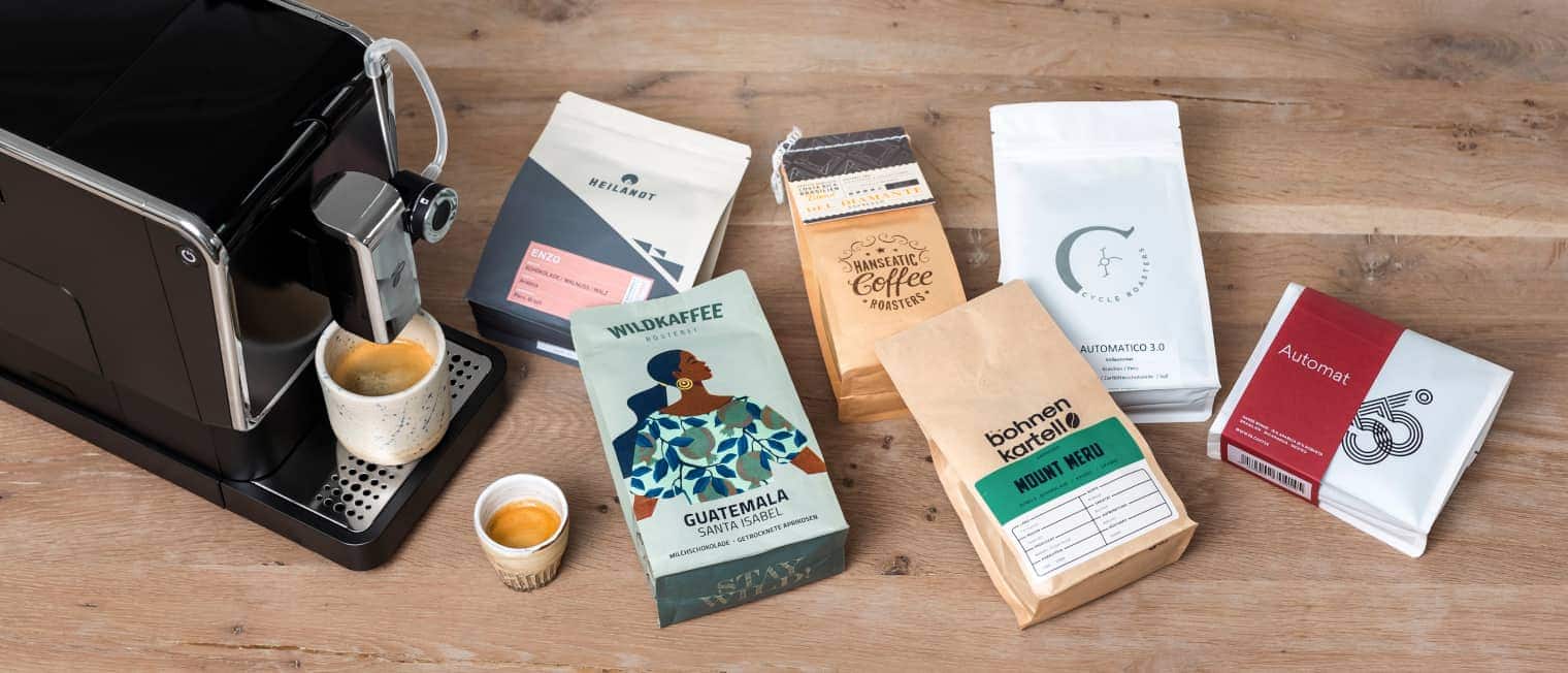 Eine große Auswahl an Specialty Coffee liegt auf Tisch neben einem Vollautomaten.