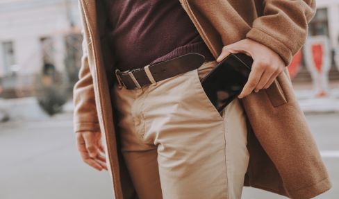 Nahaufnahme von einer beigen Softshellhose. Ein Mann steckt sein Portemonnaie in die Tasche seiner Hose.