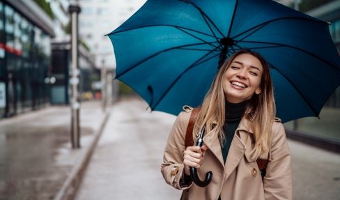 So modisch kann er sein: Eine Frau im Mantel hält einen großen blauen Regenschirm in ihrer Hand.