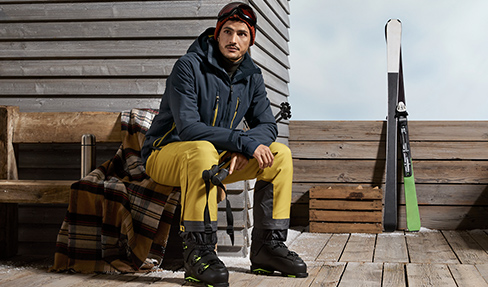 Zum Skifahren hat der junge Mann nicht nur Winterfeste Kleidung an, sondern trägt auch die richtige Ausrüstung bei sich.