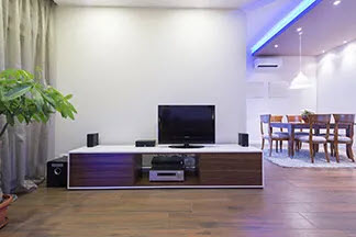 Praktische Abstellfläche: Ein edles Lowboard mit weißer Platte und dunklen Holzelementen auf dem ein Fernseher, kleine Boxen und weiter Multimedia-Geräte stehen.