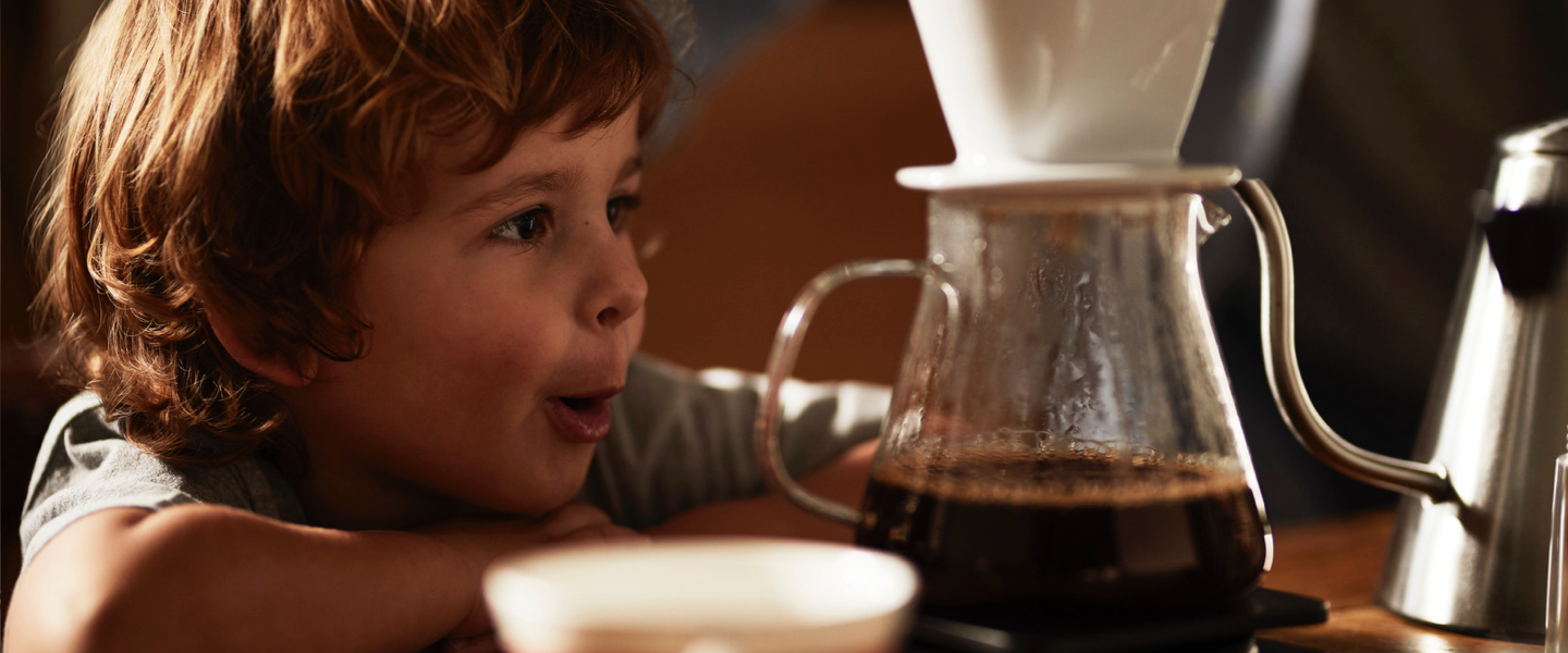 Ein kleiner Junge schaut zu, wie ein Kaffee mit einem Keramikfilter in eine Glaskanne aufgebrüht wird