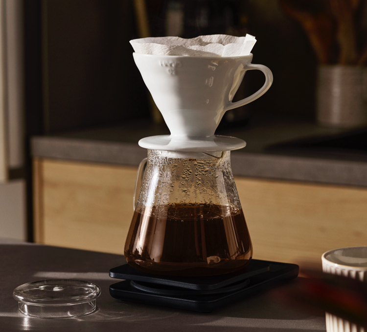 Kaffee läuft durch einen Keramikhandfilter in eine Glaskanne
