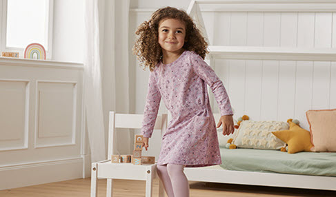 Einfach im Trend: Ein kleines Mädchen in einem rosa Kleid mit langen Ärmeln läuft durch ihr Kinderzimmer.