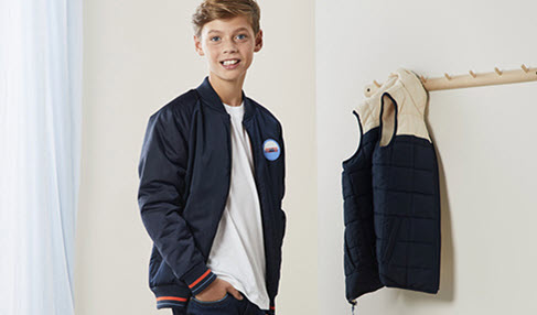 Kreative Designs: Ein Teenager steht lässig in einer dunkelblauen Bomberjacke vor einer Garderobe.
