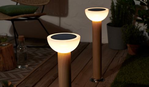 Gartenbeleuchtung richtig einsetzten: An einem Holzzaun stehen runde Gartenlampen, die kleine Zierbäume anstrahlen.