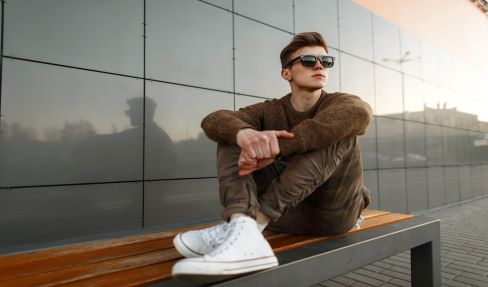Super bequem: Ein Mann trägt eine beige Funktionshose und eine Sonnenbrille und sitzt in der Sonne auf einer Bank.