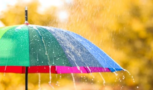 So verwendet man seinen Regenschirm richtig: Von einem regenbogenfarbenen Regenschirm prallen Regentropfen ab.