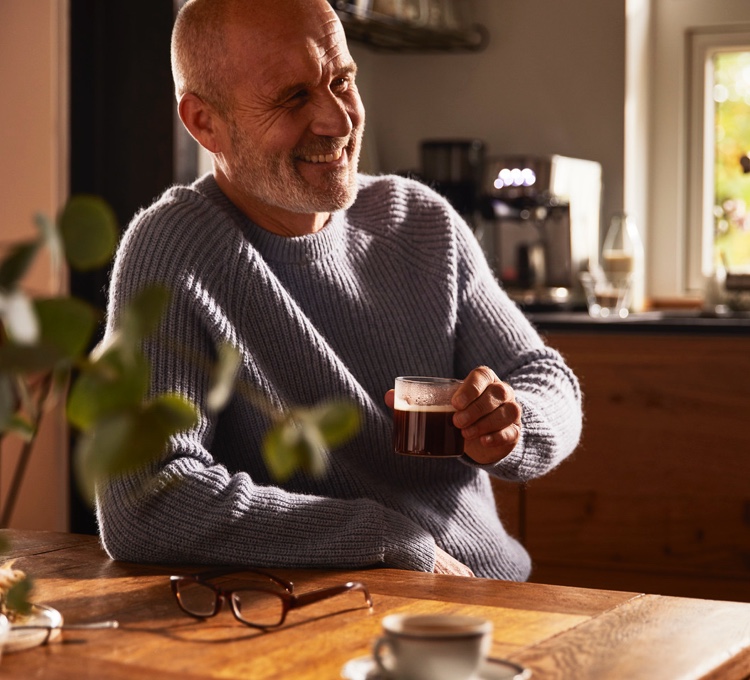 Ein Mann lehnt an einem Tisch und trinkt seinen Espresso.