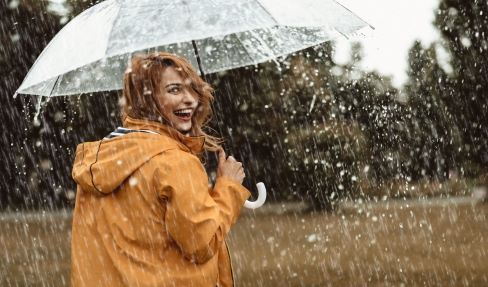 Eine Frau im gelben Regenmantel hält einen durchsichtigen Regenschirm um sich vor dem Regen zu schützen.