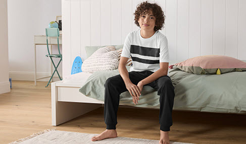 Super weich: Ein Junge sitzt in einer schwarzen Webehose auf seinem Bett.