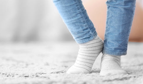 Ein Teenager läuft mit weiß-grau-gestreiften Sneakersocken über einen weißen Teppich.