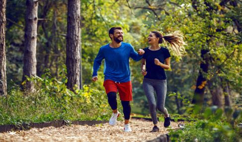 Eine Frau und ein Mann sind zusammen im Wald laufen. er trägt ein blaues Langarmshirt und eine rote Sportshorts.