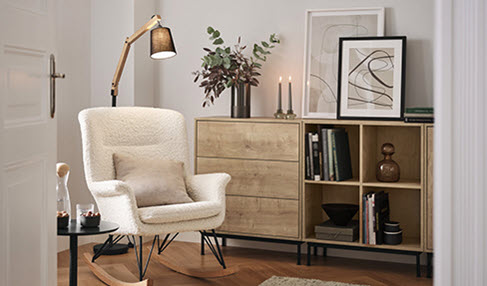 In einem Wohnzimmer steht ein weißer Sessel vor einem Holzregal.