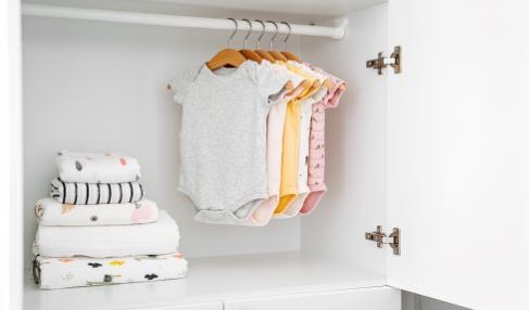 Viel Stauraum: In einem Kinderkleiderschrank hängen an einem Bügel Strampelanzüge in verschiedenen Farben.
