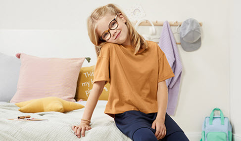 Ein junges Mädchen sitzt auf ihrem Bett und trägt ein gelbes weites Schlafshirt.